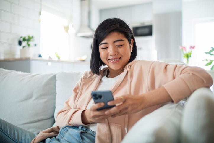 Close up of a Young woman using a smart phone while sitting on a couch in a living room